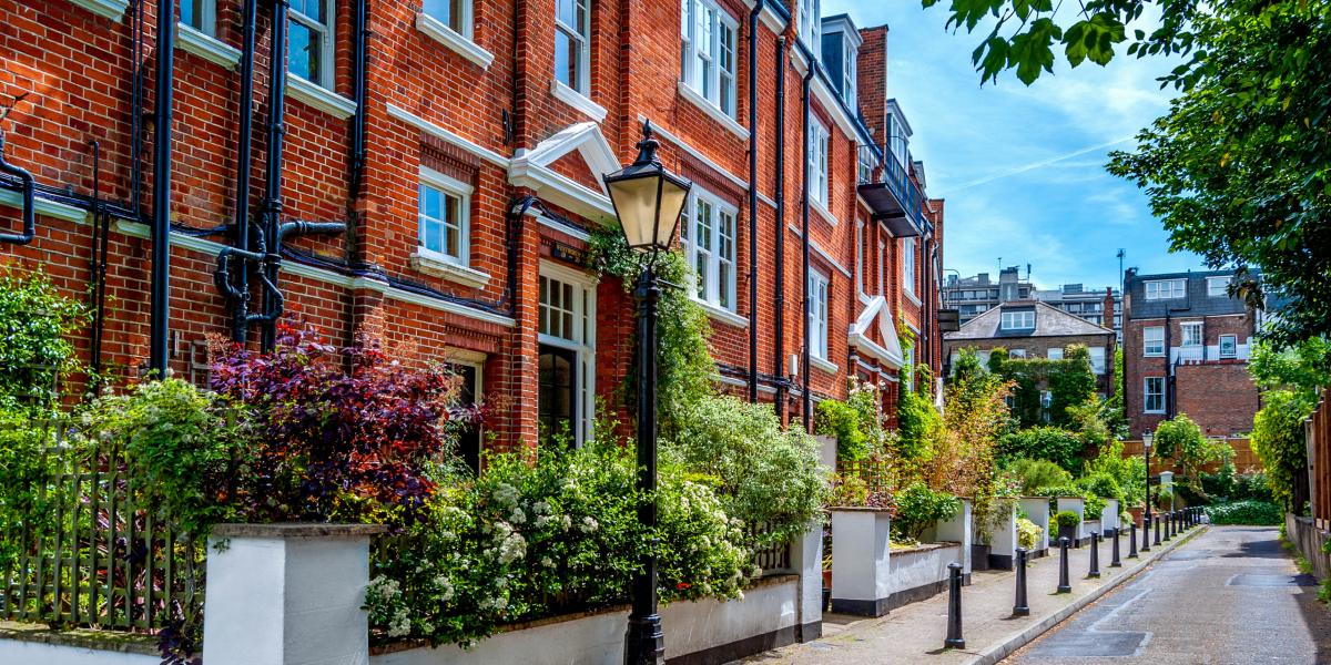 Residential street with red-brick houses and bushes of colorful flowers in Hampstead area, north London, England.